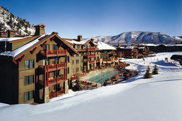 Ritz Carlton Club, Aspen exterior view of the green with red accent resort and the pool surrounded by snowy landscape